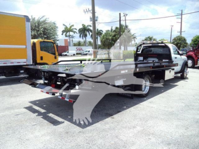 Ram 5500 rollback tow truck showing long flatbed with white cab and black bed, VIN visible, dealership lot in background.