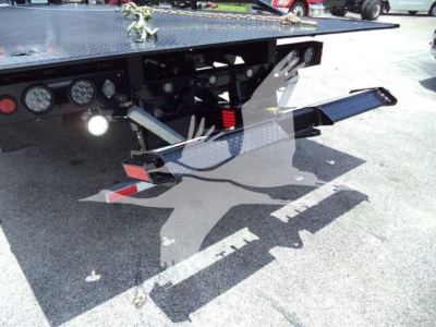 Ram 5500 rollback truck rear with hydraulic flatbed and wheel chock, showing undercarriage, toolkit, and rear lighting.