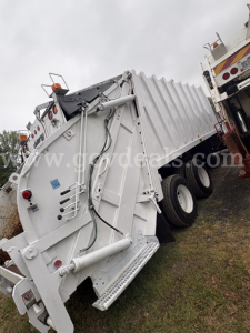 Side view of a large white Sterling LT8500 garbage truck hopper with rear wheels and hydraulic system visible.