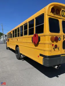 School bus rear quarter view showing yellow Body, windows, tail lights, exhaust, and a red stop sign on the side.