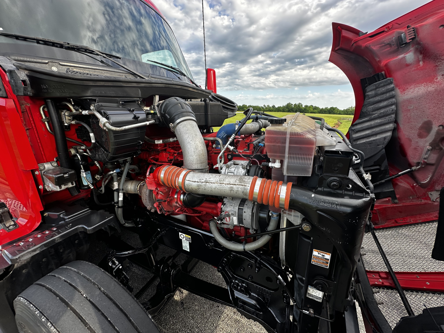 Kenworth T680 engine bay view showing engine components and intake tubing under open hood.
