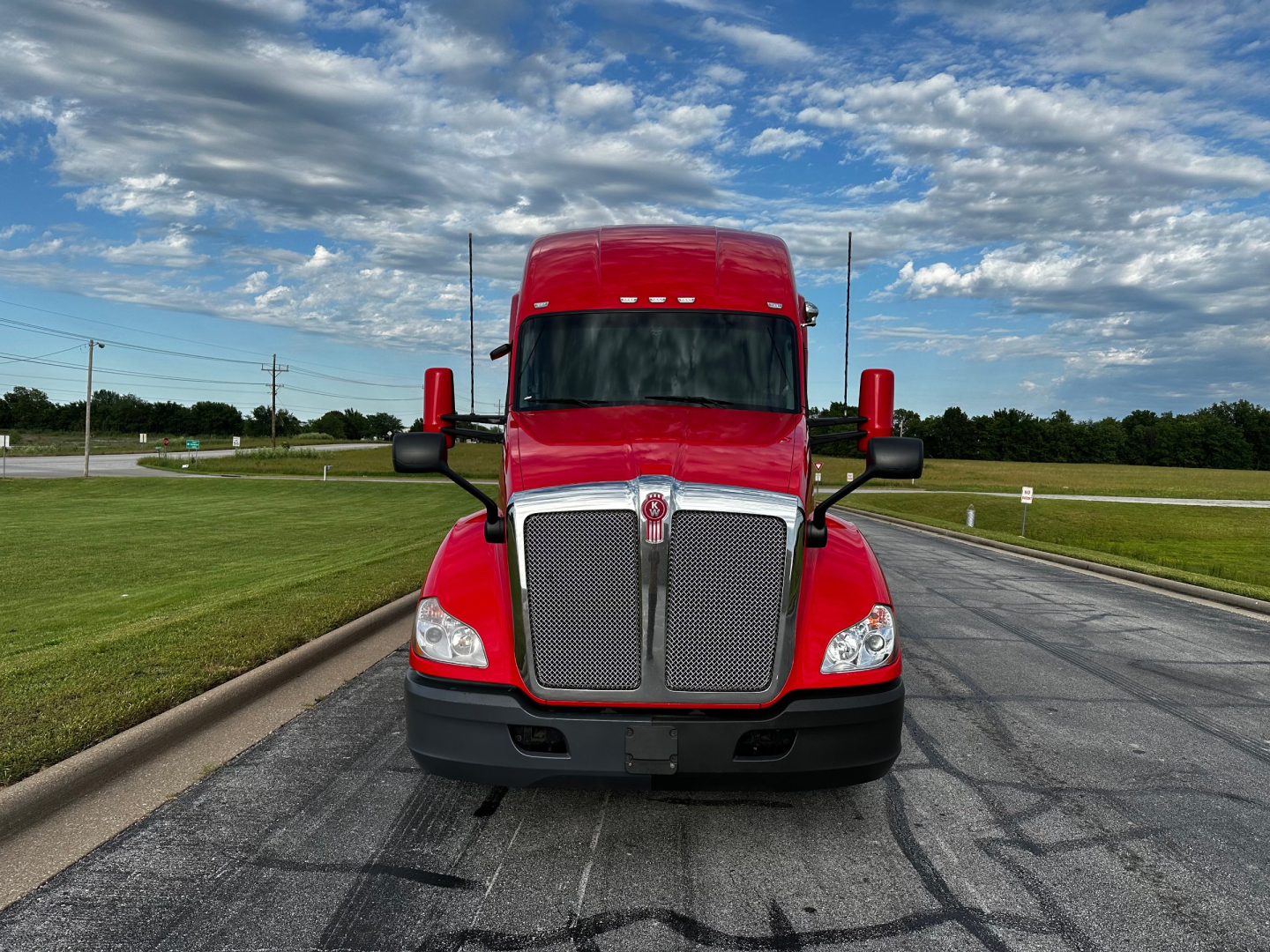 Kenworth T680 truck front view showing large chrome grille, red cab, black bumper, and side mirrors.