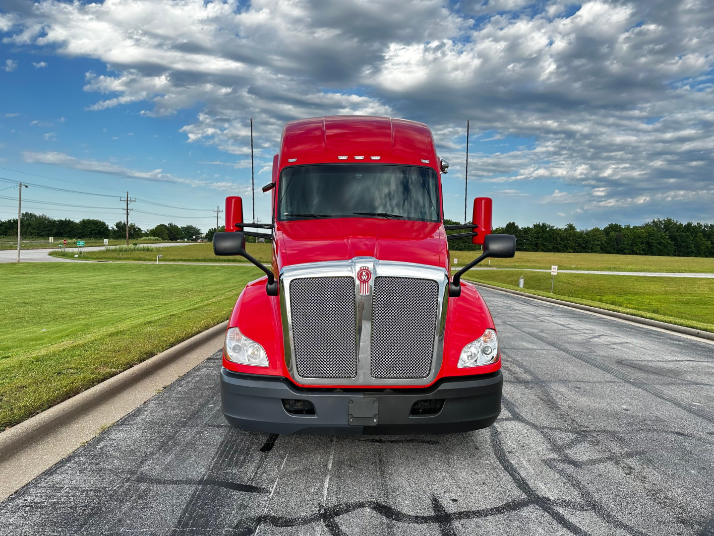 Kenworth T680 truck front view showing red cab and large grille with chrome surround and black bumper.