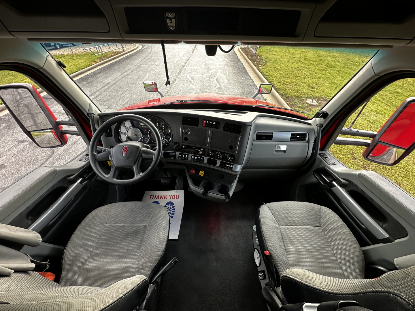 Kenworth T680 cab interior view with steering wheel, dashboard, and two front seats, driver-side door open
