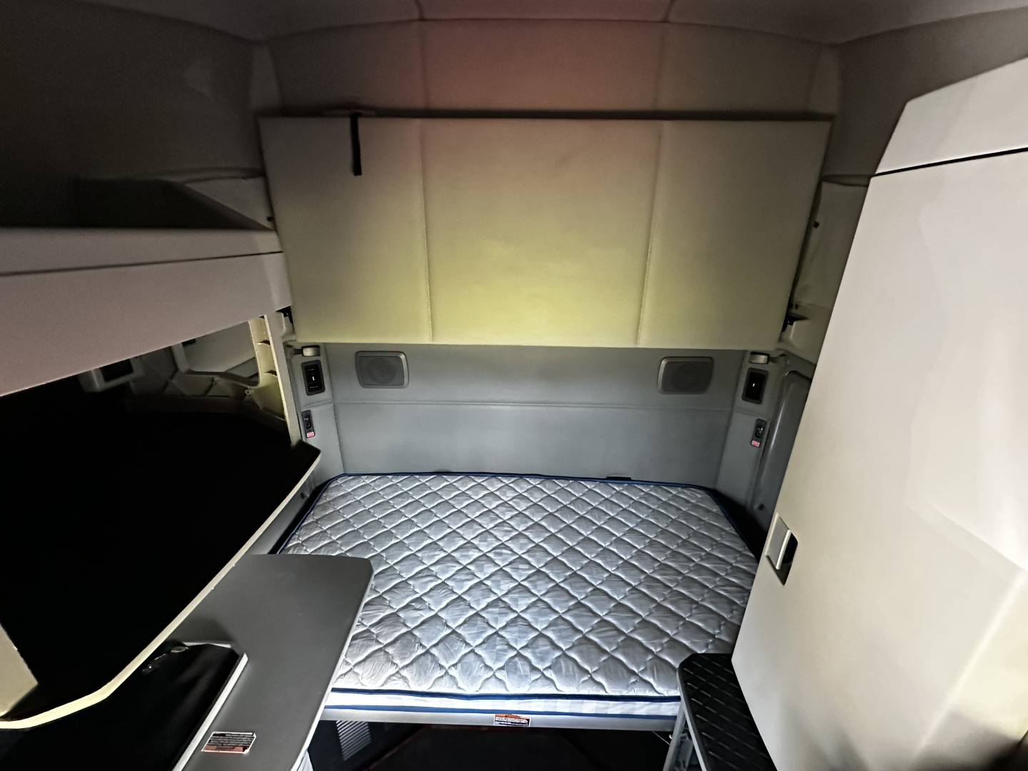 Kenworth T680 sleeper cab interior with a quilted mattress platform in the cargo area, view of the rear cabin walls and storage area.