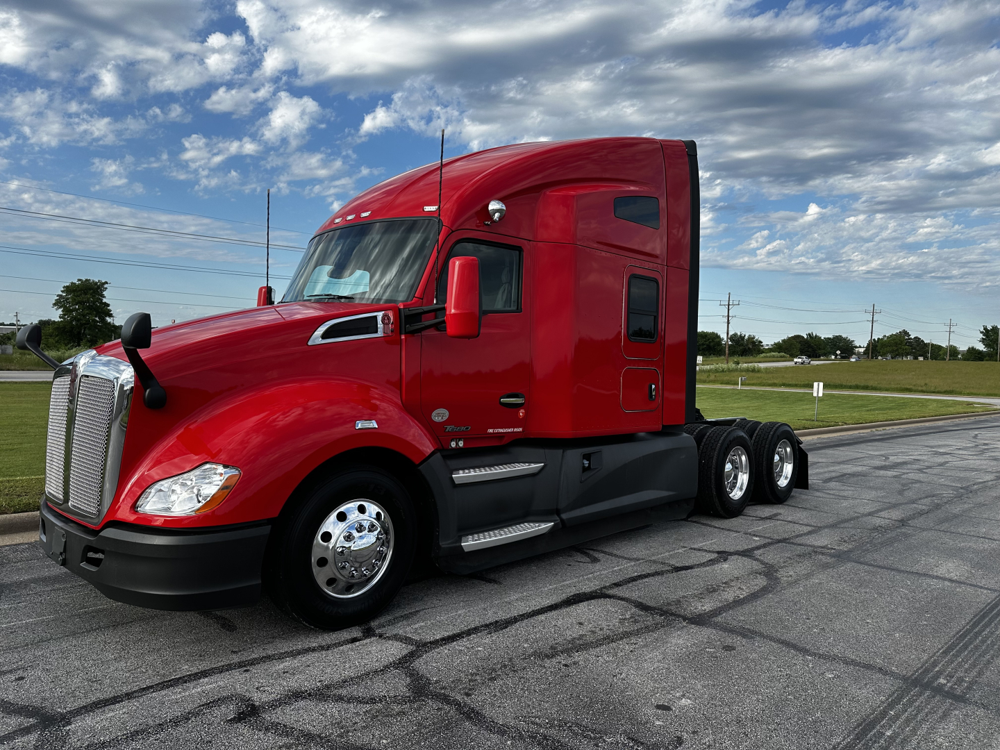 Kenworth T680 tractor in red, side view showing chrome fuel tanks, steps, and dual rear axles.