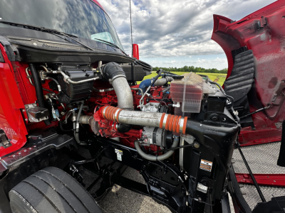 Kenworth T680 engine bay view showing engine components and intake tubing under open hood.