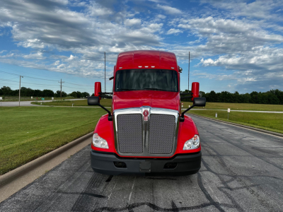 Kenworth T680 truck front view showing large chrome grille, red cab, black bumper, and side mirrors.