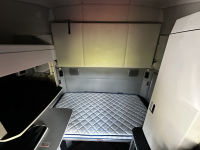 Kenworth T680 sleeper cab interior with a quilted mattress platform in the cargo area, view of the rear cabin walls and storage area.