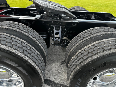 Truck chassis undercarriage showing dual rear axles and suspension components with tires and wheels.