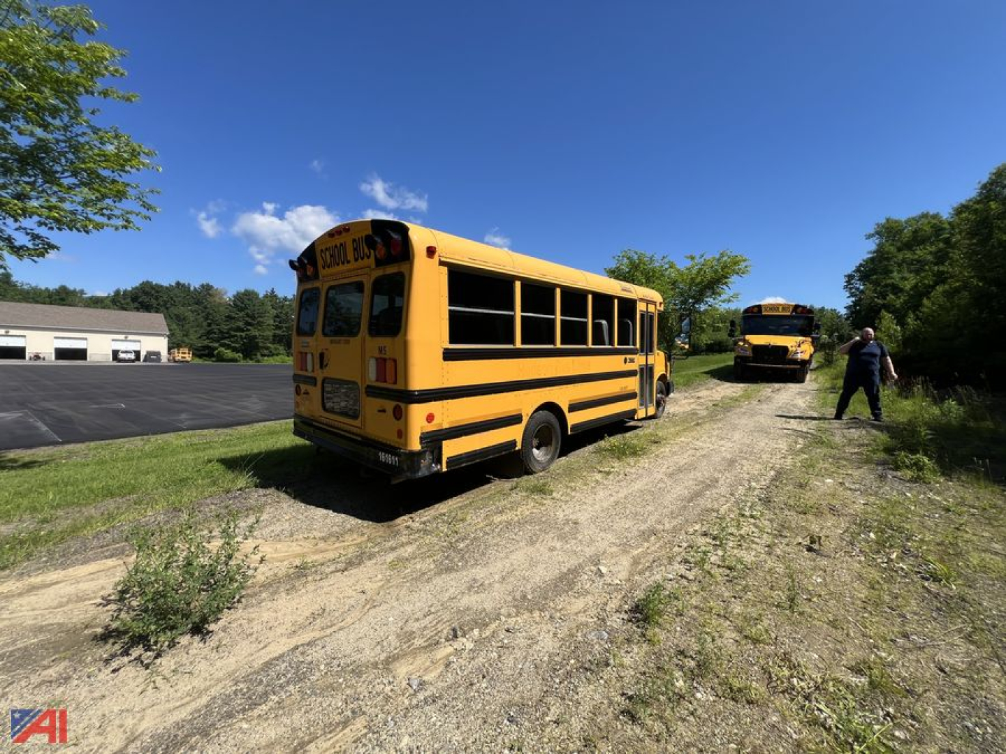 Yellow Chevrolet Express school bus in a rural lot, rear and side view, another bus in background.