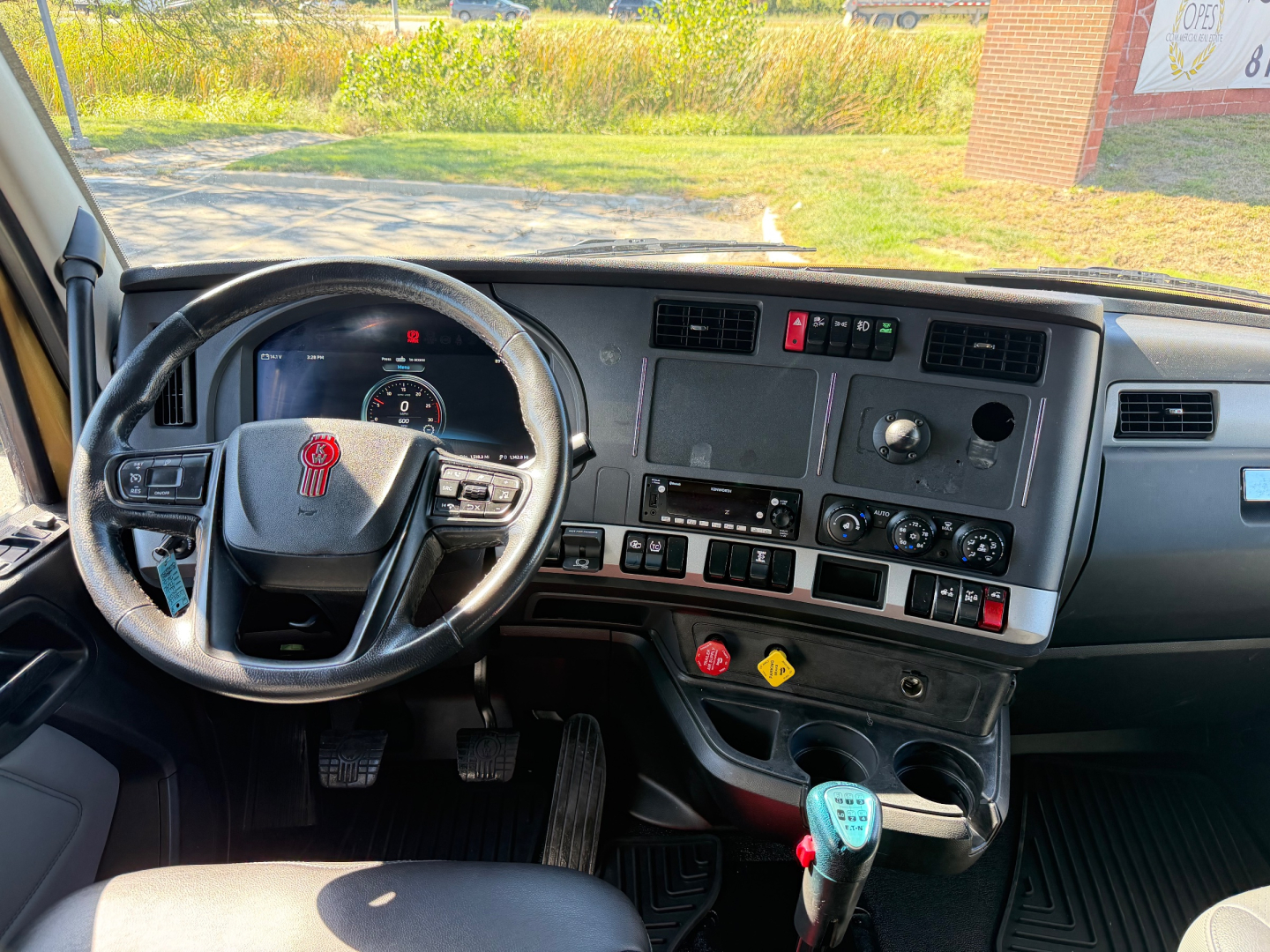 Truck cab interior of a Kenworth T680 with steering wheel left, dashboard controls, gear shifter, and center console with multiple switches and gauges.