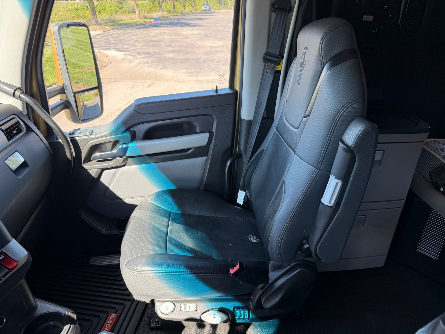 Interior driver seat of a Kenworth T680 cab showing steering wheel, dash, and passenger seat with storage cabinet in background.