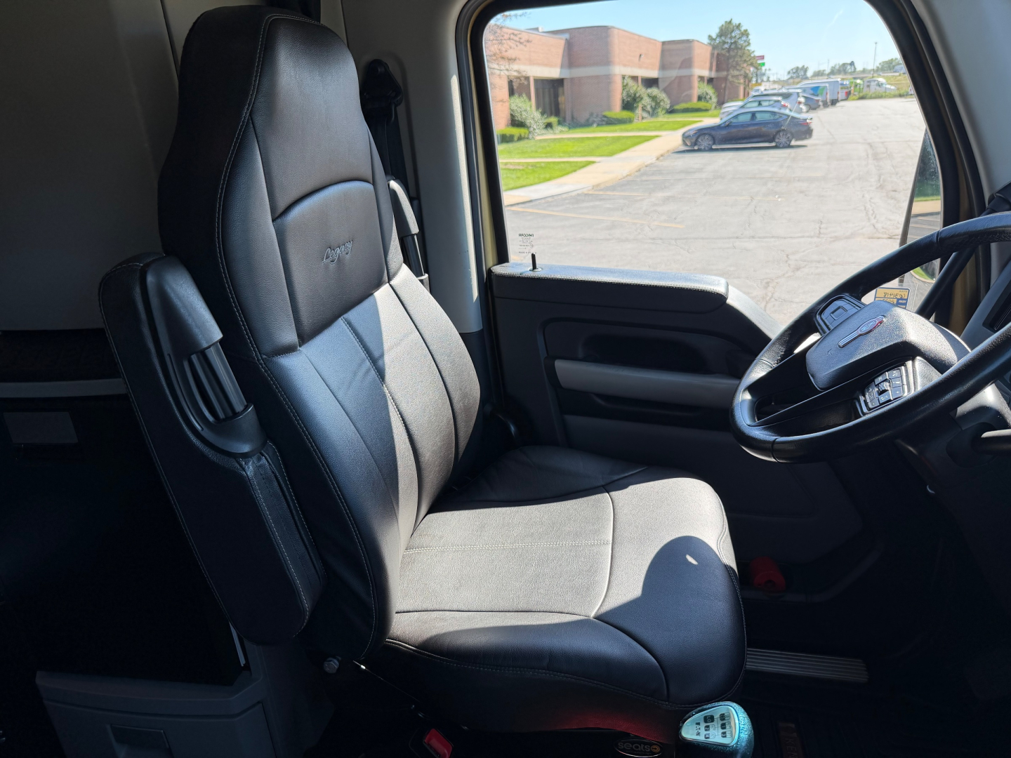 Kennworth T680 truck interior front seat and steering wheel view with dashboard and window; black leather seat with armrest.