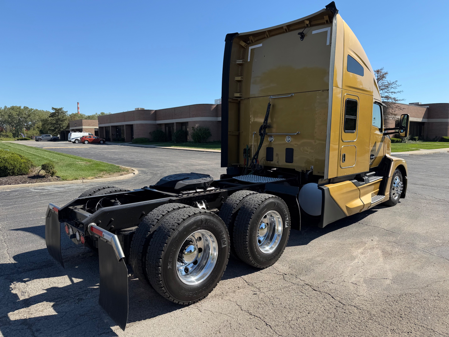 Kenworth T680 tractor in a yard with a sleeper cab, rear triple-axle configuration visible, yellow cab, fuel tanks, and fifth-wheel; no visible text legible on components.