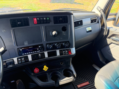 Kenworth T680 dash view showing center console with climate controls, radio, and cup holders; steering wheel visible on left, passenger side with glove compartment.