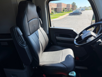 Kennworth T680 truck interior front seat and steering wheel view with dashboard and window; black leather seat with armrest.