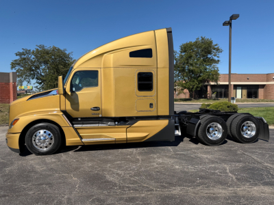 Kenworth T680  truck side view in beige color with sleeper cab and triple rear axles.