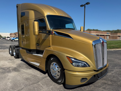 Kenworth T680 sleeper cab tractor in metallic gold showing front grille, chrome wheels, side step, and dual rear axles. No visible text on the image beyond the truck design.