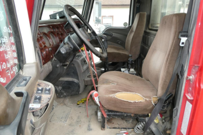Interior of a 2005 Mack CHN613 daycab with a torn driver seat, steering wheel, dashboard, and gear shifter visible.