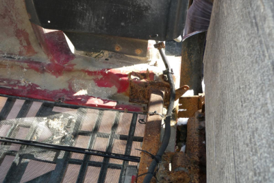 Mack truck chassis area showing rusty components and wiring near floor and frame.