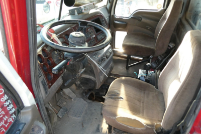 Truck cab interior showing steering wheel and dashboard of a Mack CHN613 conventional daycab, worn cloth seats, driver seat with tear.