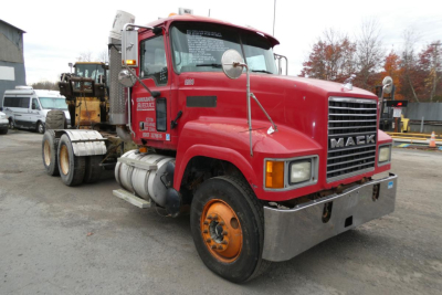 Mack CHN613 conventional daycab truck in red with side exhaust stack and orange wheels, front grille and bumper visible.