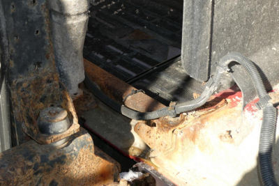 Mack CHN613 engine bay area showing hoses and rusted frame with battery tray and wiring.