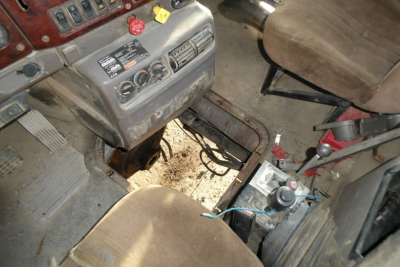Interior of a 2005 Mack CHN613 daycab showing dashboard controls, steering column, and gear area with wiring and seating; visible label panels and pedals.