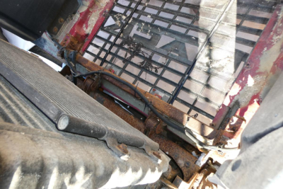 Truck cab interior showing metal grate and exposed frame with visible rust; window grid and part of a seat on a Mack CHN613.