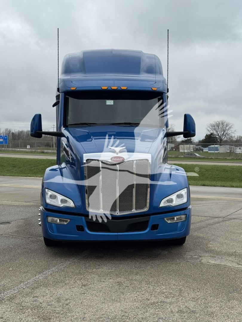 Front view of a blue 2023 Peterbilt 579 conventional sleeper truck showing grille, headlights, and two tall antennae on the hood.
