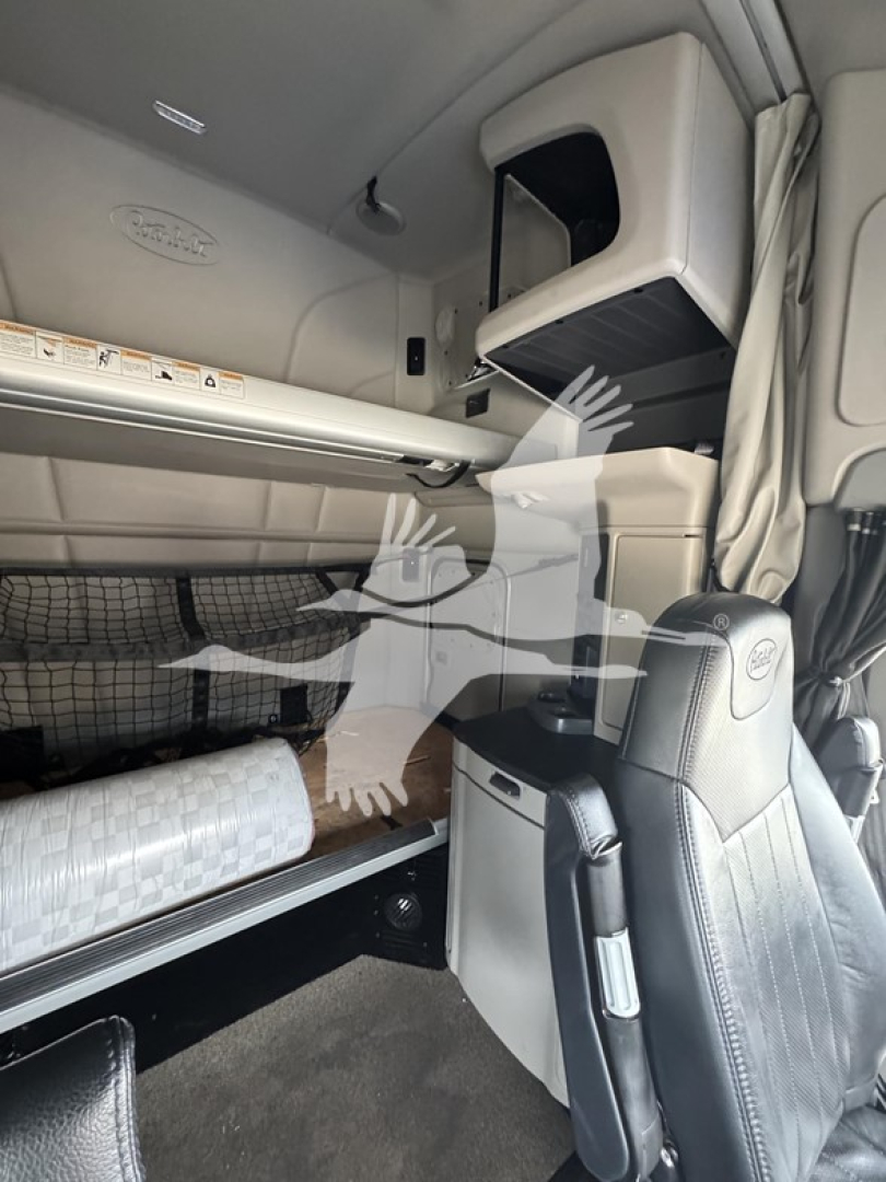 Truck sleeper cab interior showing bunk bed area and passenger seat, Peterbilt branding on panels, storage compartments, and air deflector vents.