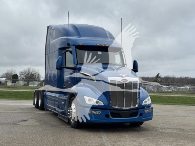 Truck front view of a blue 2023 Peterbilt 579 conventional sleeper with chrome grille and large aerodynamic mirrors.