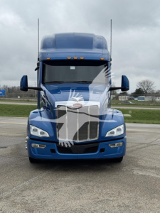Front view of a blue 2023 Peterbilt 579 conventional sleeper truck showing grille, headlights, and two tall antennae on the hood.