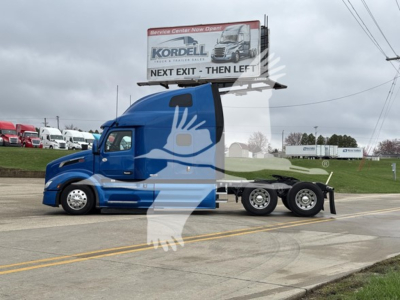 Peterbilt 579 truck tractor in blue with a trailer shown from side, signage atop cab and billboard visible.