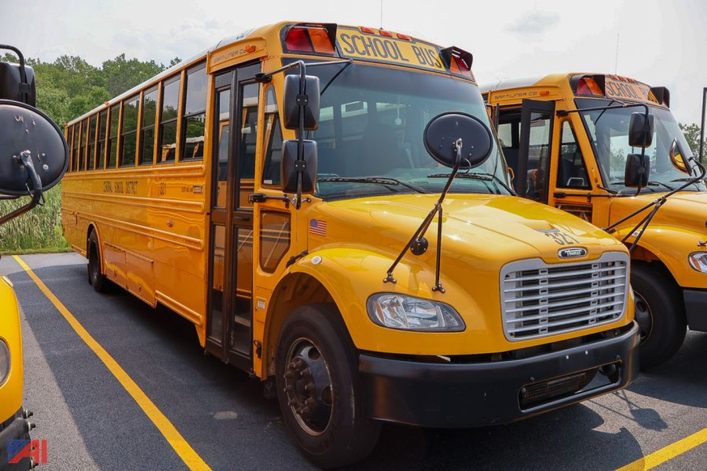 Front and side view of a yellow Freightliner Thomas Saf-T-Liner school bus with 'SCHOOL BUS' signage on top, adjacent bus in background.