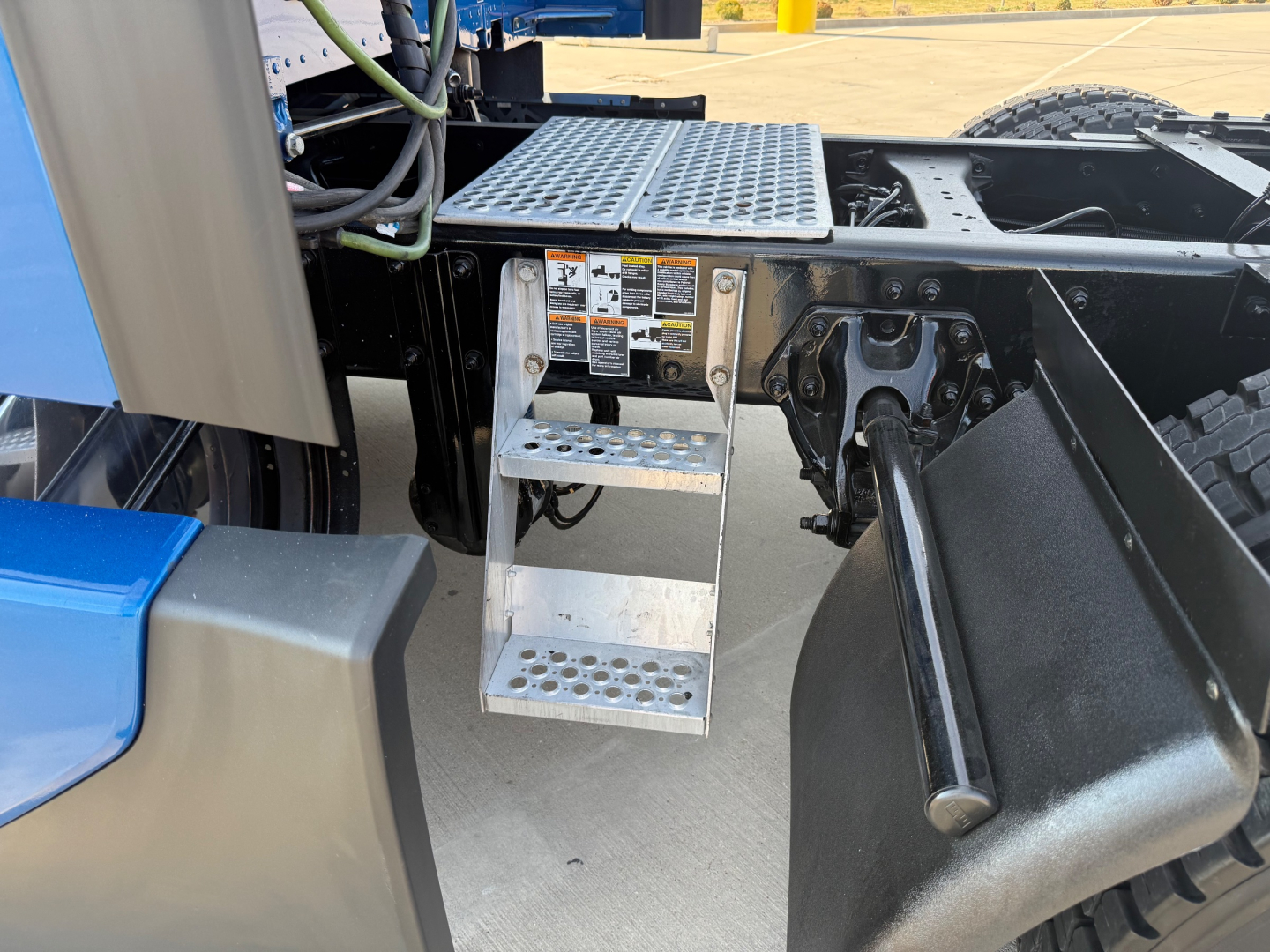 Kenworth T680 chassis area with aluminum work steps, access plate, and surrounding drivetrain components visible.