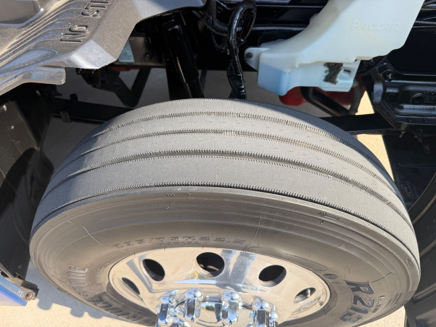 Kenworth T680 front wheel area showing single drive tire, wheel cover, and part of brake air reservoir and coolant reservoir.