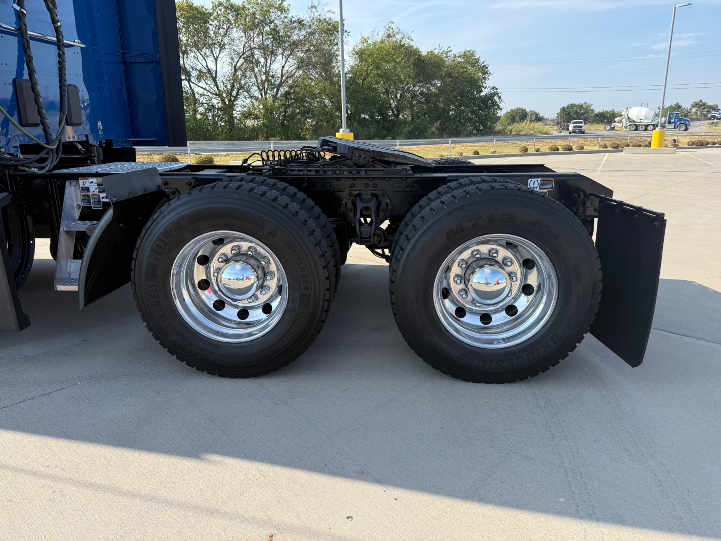 Kenworth T680 rear dual-axle wheels with chrome hubcaps and mud flaps, chassis frame and tires visible.
