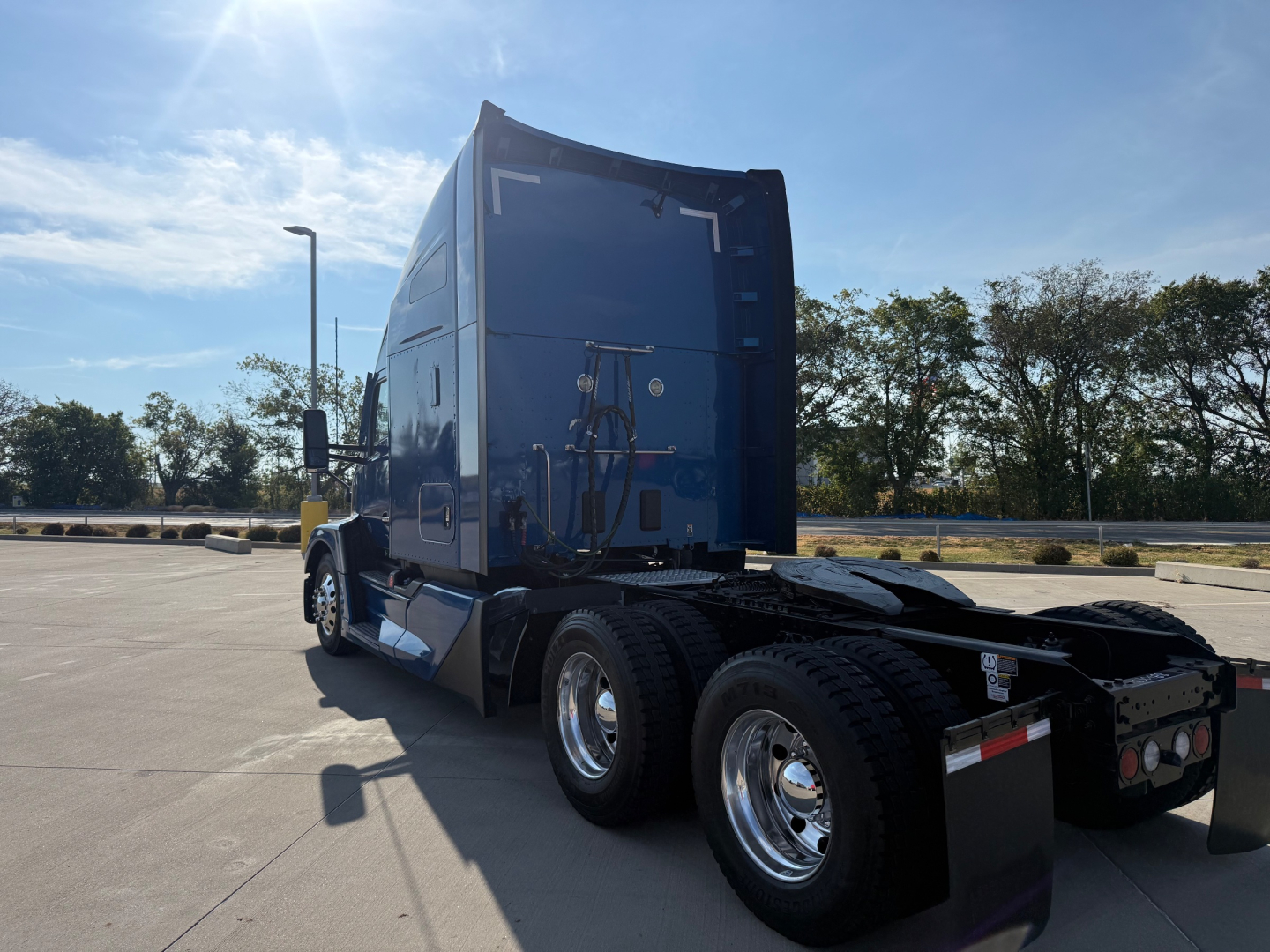 Kenworth T680 tractor sleeper cab rear view showing dual rear axles and fifth wheel, blue paint, chrome fuel tanks, and rear lights.