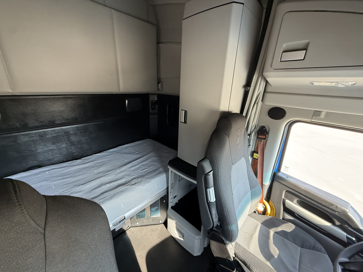 Truck sleeper cab interior of a Kenworth T680 with bunk bed and nearby swivel chair, storage cabinet, and dashboard visible.