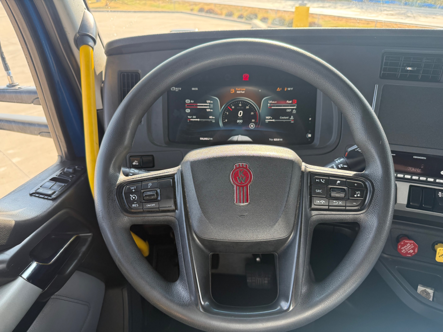 Kenworth T680 steering wheel and dashboard with digital gauge cluster visible; interior view of the cab showing steering wheel with red Kenworth emblem and various control buttons.