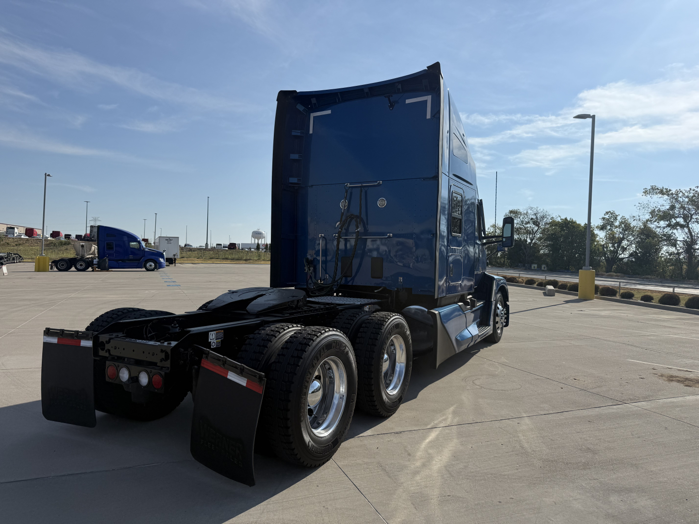 Kenworth T680 semi-truck in a parking lot, rear view showing triple axle and sleeper cab.