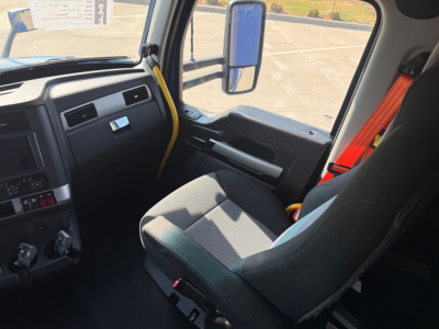 Truck cab interior of a Kenworth T680 showing steering wheel, dashboard, and front passenger seat with orange seat belt in view.