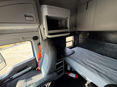 Kenworth T680 truck cab interior showing sleeper bunk area, seating, overhead compartments, and a metal shelf with a small storage bin.