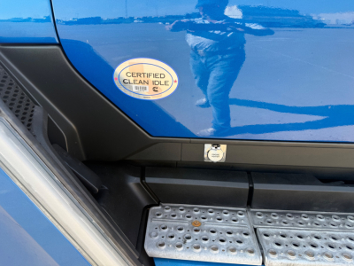 Kenworth T680 side step area with Certified Clean Idle sticker on blue door panel and metal running board.