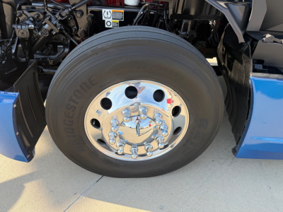 Wheel and front suspension of a 2023 Kenworth T680 truck showing Bridgestone tire and polished steel rim with lug nuts.
