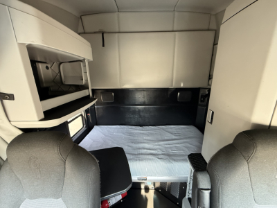 Truck cab interior of a Kenworth T680 sleeper showing a bed platform and storage compartments with text labels minimal.