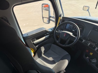 Kenworth T680 interior view showing steering wheel, dashboard, and driver seat with side window and mirror.