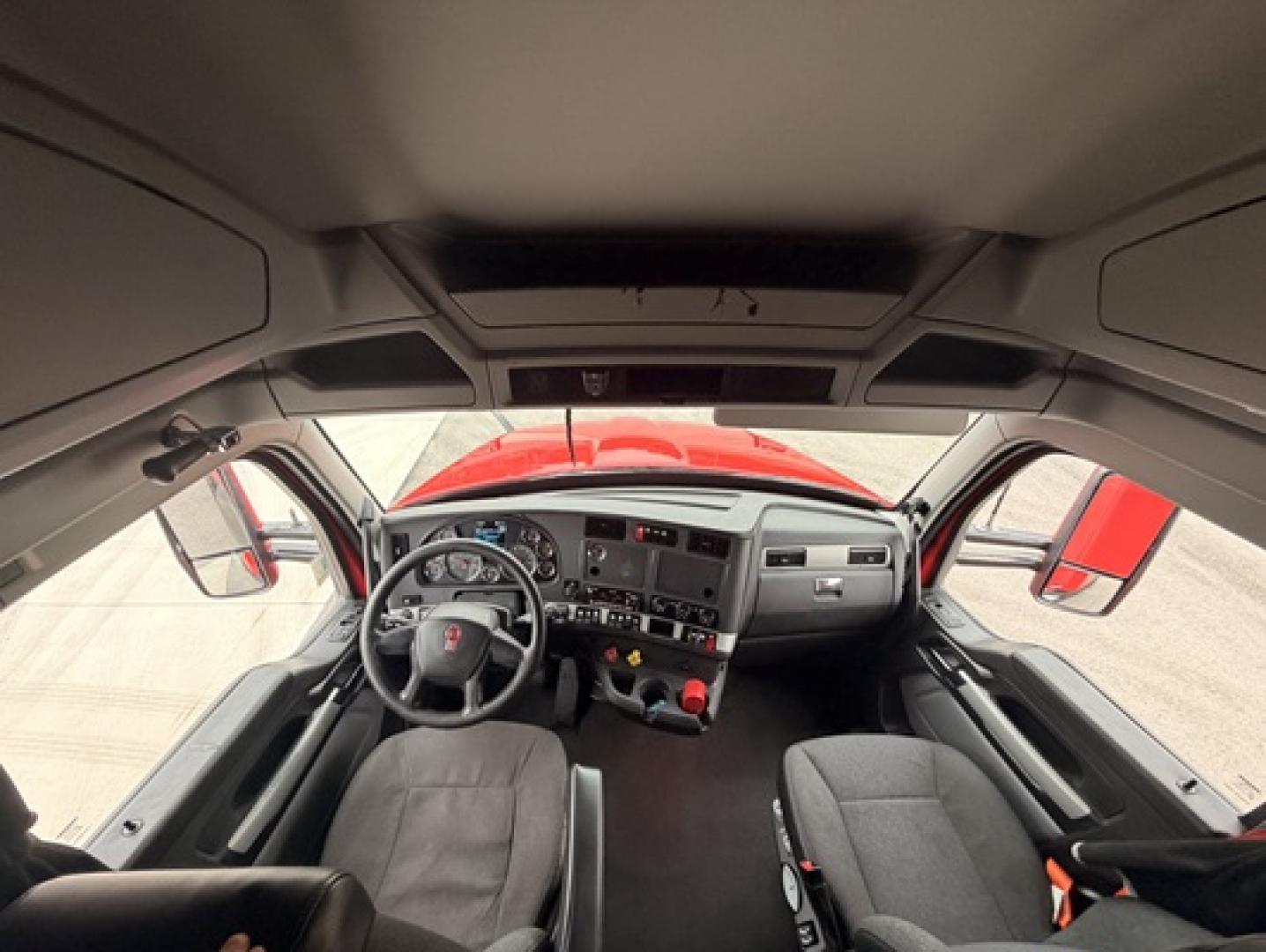 Kenworth T680 cab interior showing steering wheel dash cluster and two front seats.